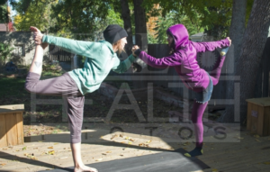 Two Women Holding Hands Standing On One Foot Each Doing Yoga